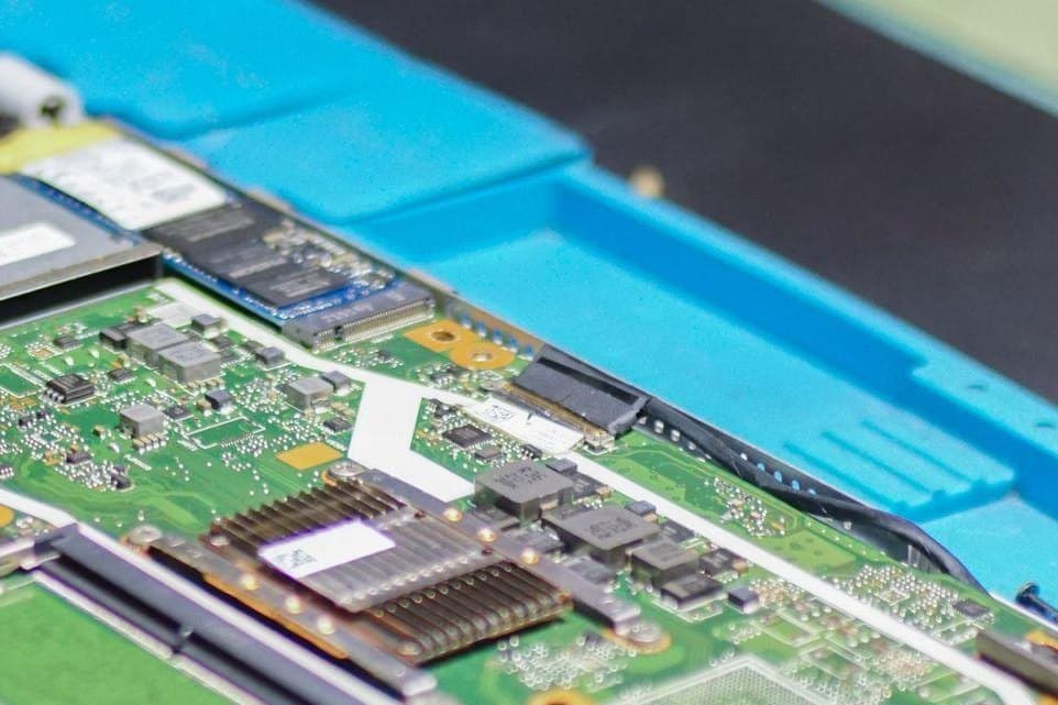 Geöffneter Laptop mit Lüfter, SSD und Mainboard auf einer blauen Reparaturmatte
